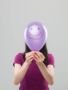 Woman holding a baloon in front of her face representing a false reality or persona. 